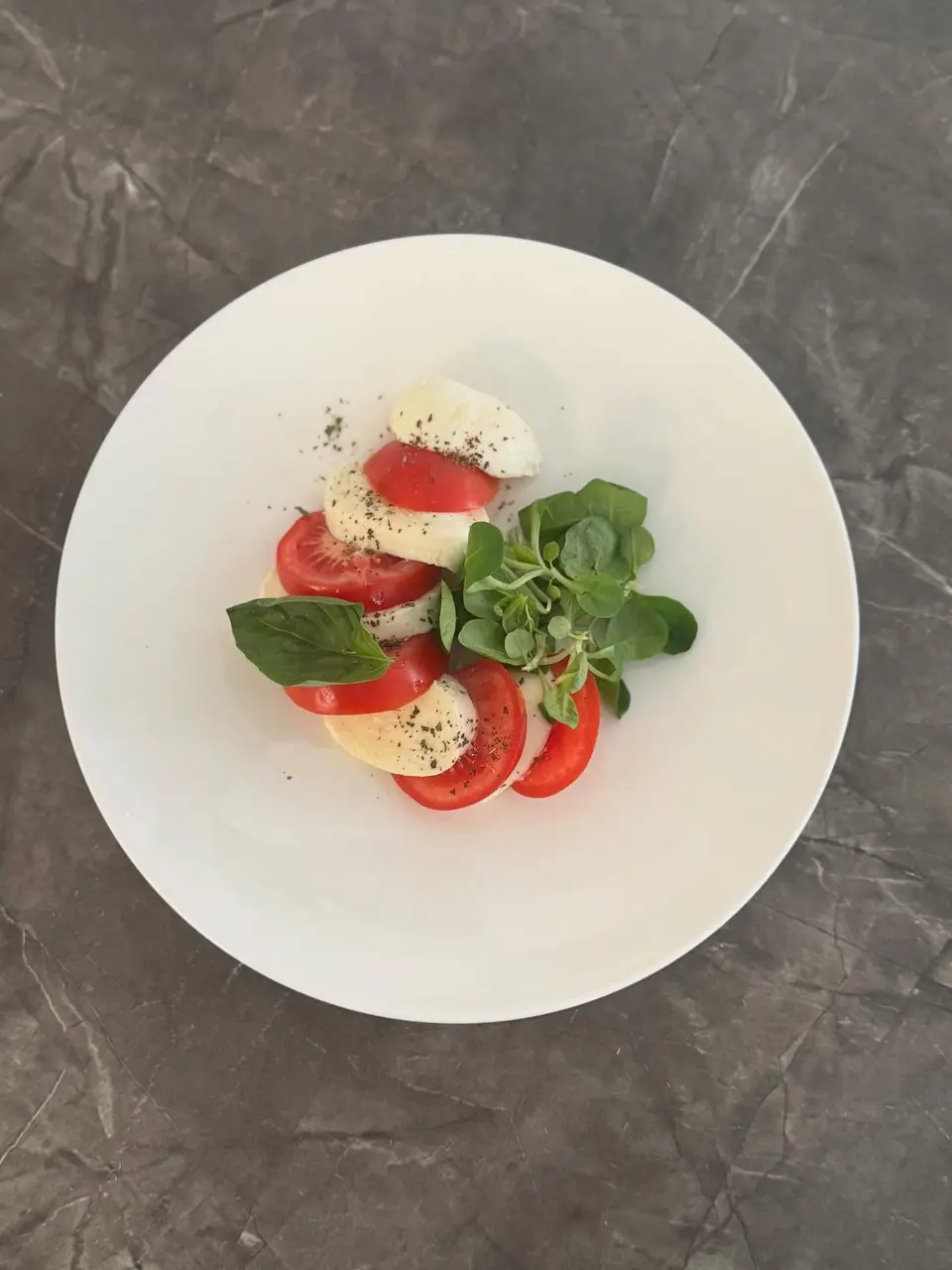 Una caprese in un piatto bianco su un tavolo di marmo grigio